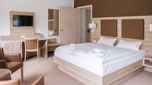 A hotel room with a bed, a desk, a chair, a TV, and a wardrobe. - Hotel zur Ostsee (Graal Mueritz)