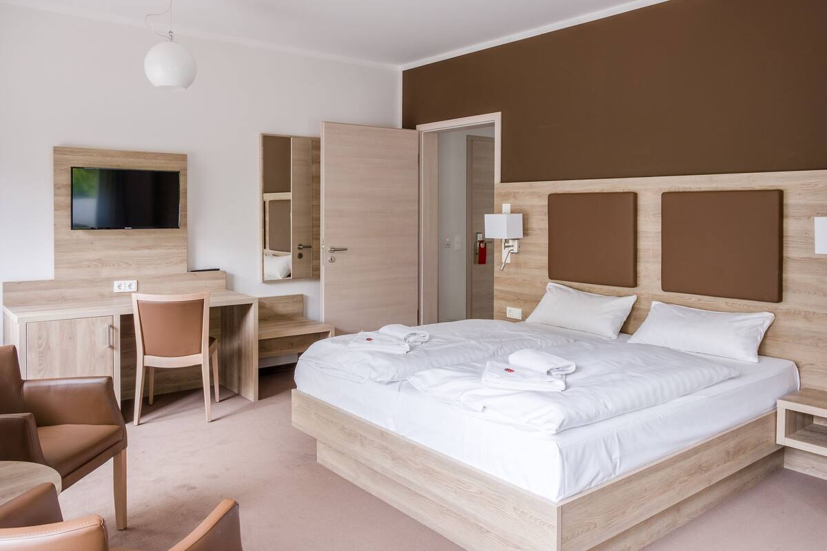 A hotel room with a bed, a desk, a chair, a TV, and a wardrobe.