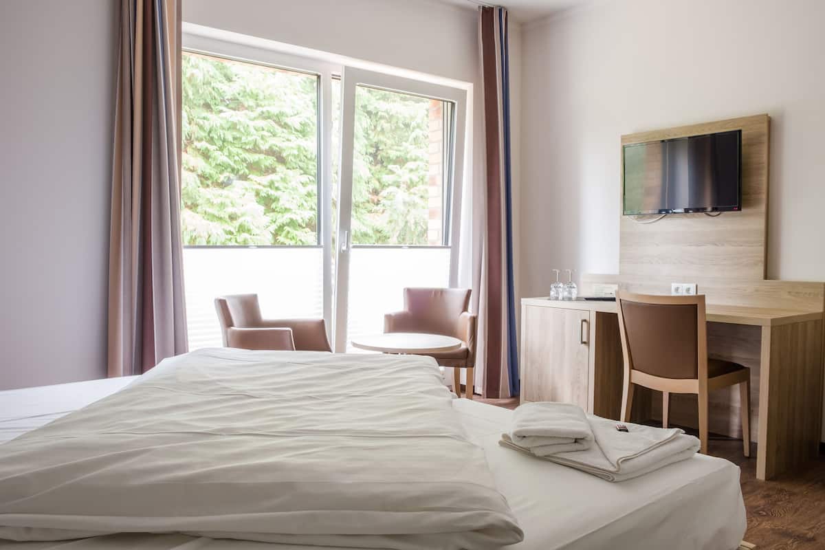 A hotel room with a bed, a desk, a chair, a TV mounted on the wall, and a window with curtains.