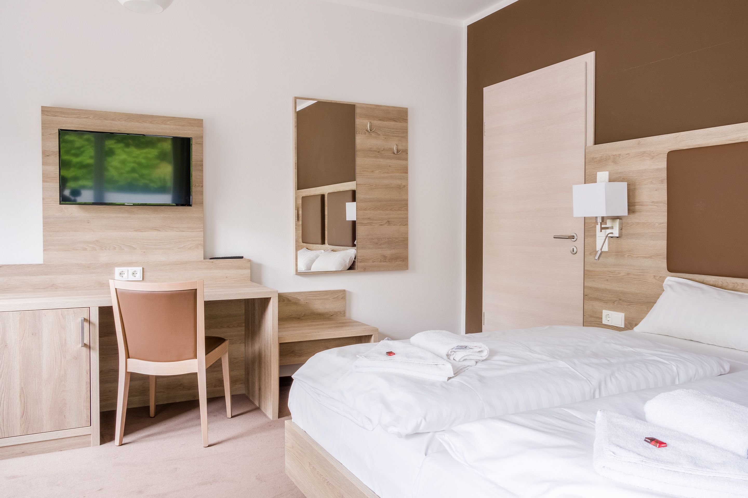 Ein modernes Hotelzimmer mit Bett, Schreibtisch, Sessel und einem an der Wand befestigten Fernseher.