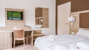Ein modernes Hotelzimmer mit Bett, Schreibtisch, Sessel und einem an der Wand befestigten Fernseher.