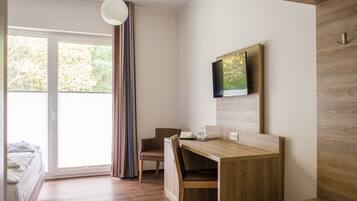 Una habitación moderna con un escritorio de madera, una silla, una cama y un televisor fijado a la pared.