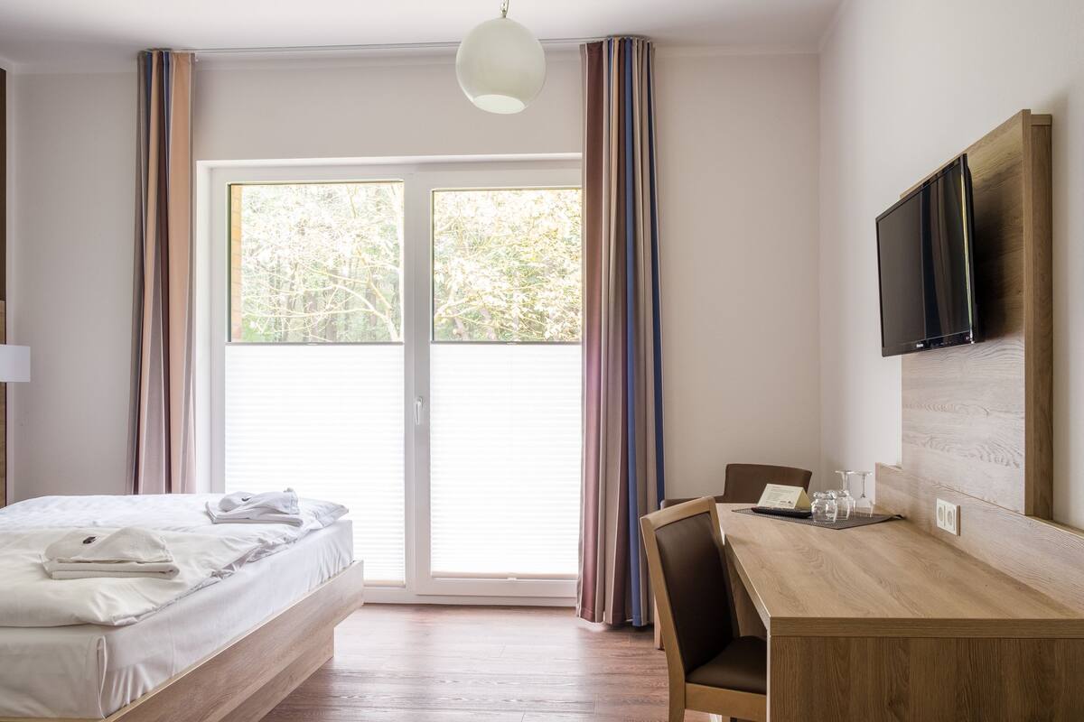 A hotel room with a bed, a desk, a chair, a television, and a sliding glass door.