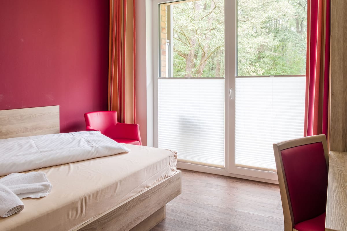 A bedroom with a bed, a red chair, and a view of trees through a window.