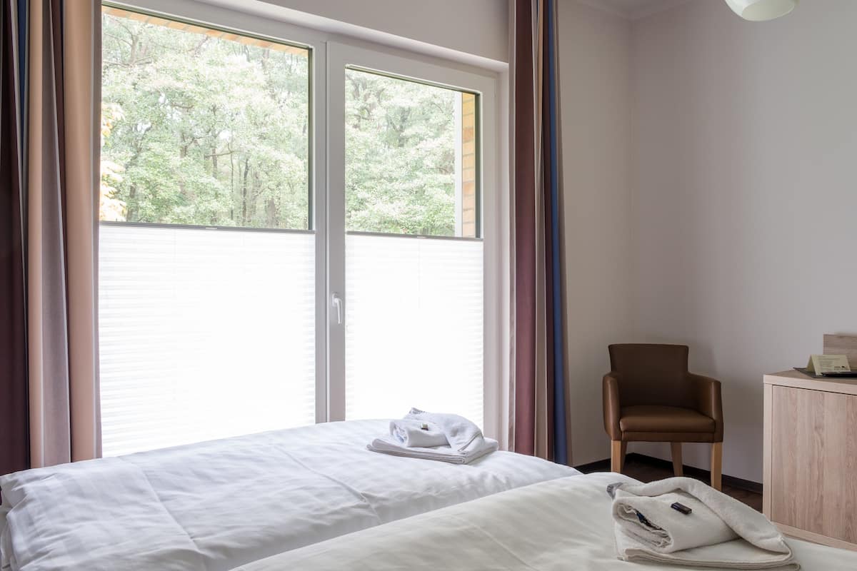 A hotel room with a bed, a chair, and a desk with a lamp.