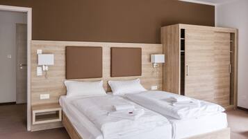 A modern bedroom with a large bed, wooden headboard, bedside lamps, and a wardrobe.