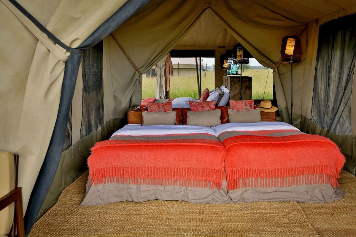 A tent with a bed, pillows, and a nightstand with a lamp.