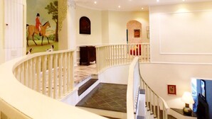 A grand staircase with a white railing, a mural of a horse rider, and a chandelier. - Casa Yvitú Blue Bird Hotel (Campos do Jordão)