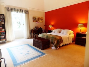 Quarto com cama, mesas de cabeceira, estante, uma janela com cortinas e um quadro na parede.