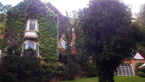 A building with ivy-covered walls and a small tower structure. - Casa Yvitú Blue Bird Hotel (Campos do Jordão)
