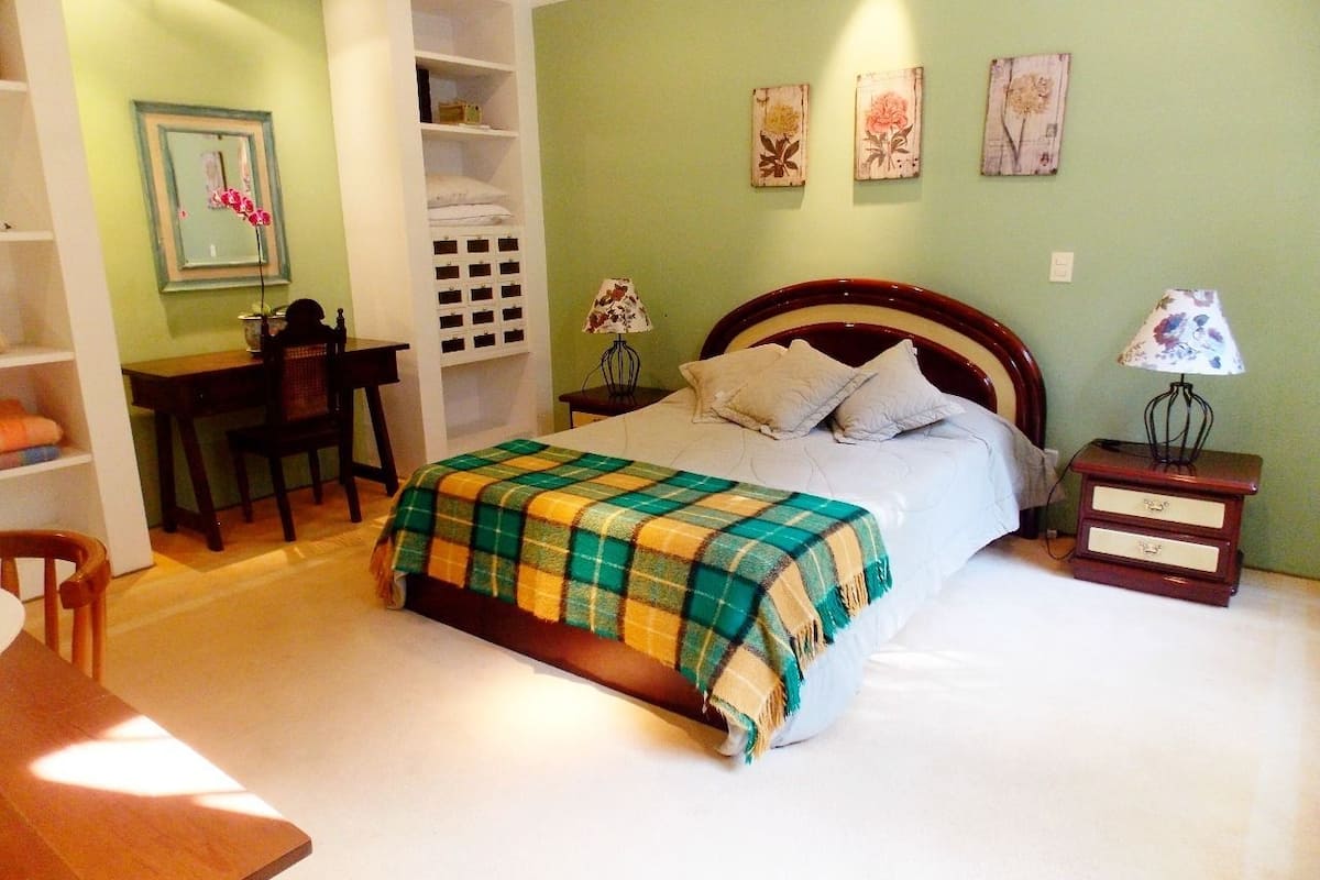 A bedroom with a bed, a desk, and a chair. There are three wall-mounted lamps and a small bedside table with a lamp.