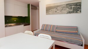 A compact room with a kitchenette, a dining area, and a sofa with striped cushions. - Villa Valentina (Jesolo)