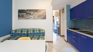 A compact kitchen with blue cabinets, a dining area with a sofa, and a wall-mounted picture. - Villa Valentina (Jesolo)