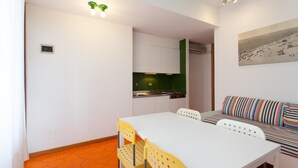 A compact living space with a dining area, kitchenette, and a sofa with striped cushions. - Villa Valentina (Jesolo)