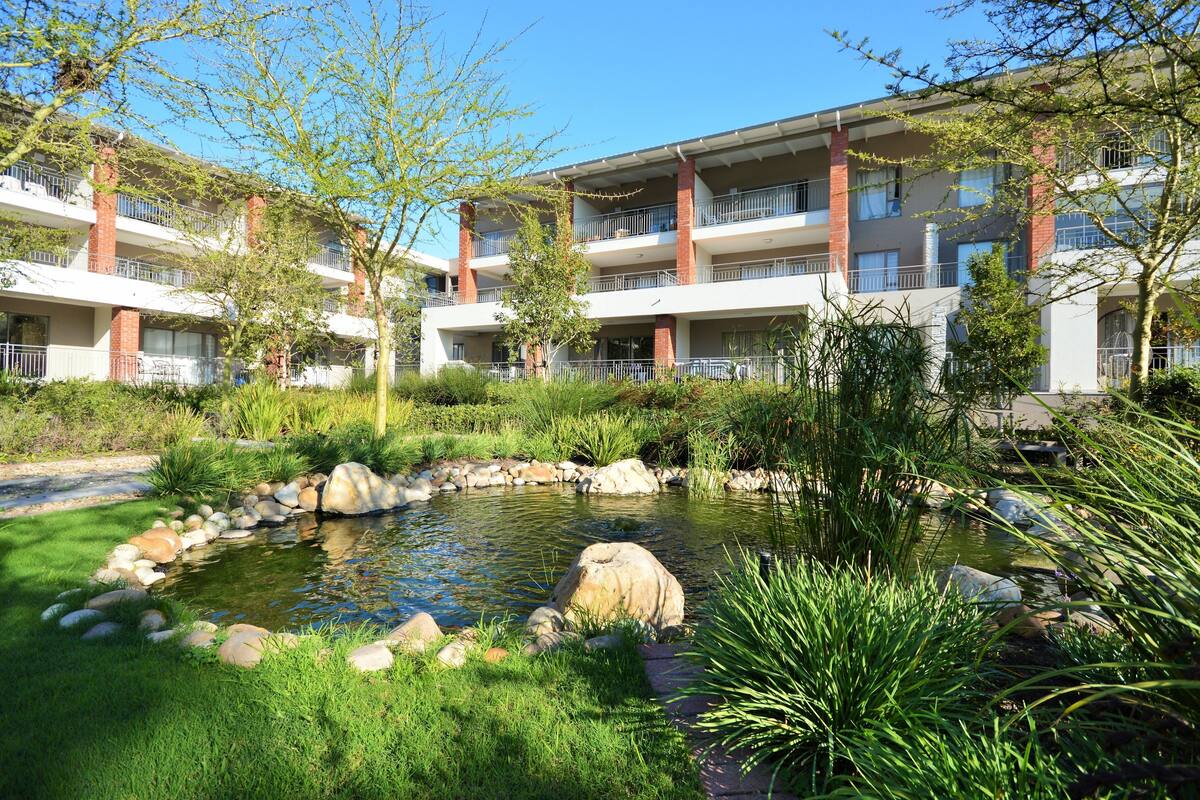 Een hotel met een aangelegde tuin, inclusief een vijver, omgeven door meerlaags gebouwen met balkons.
