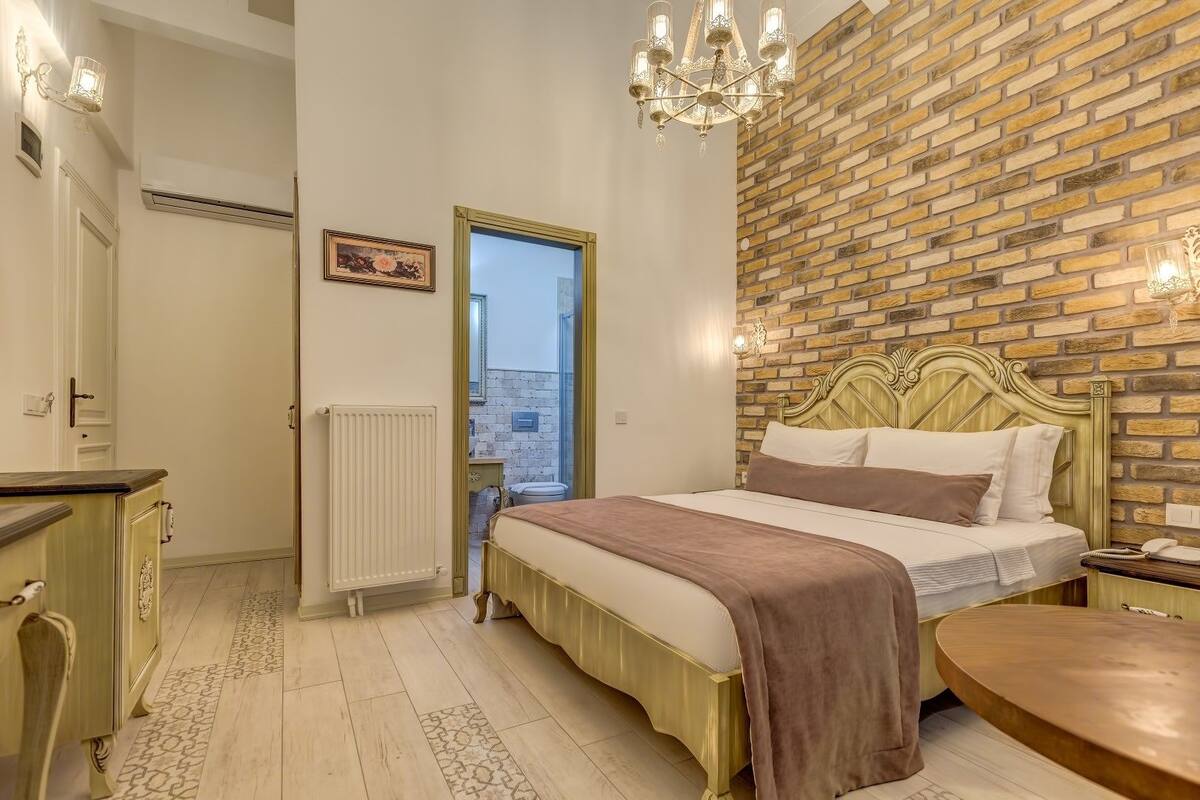 Un dormitorio con una pared de ladrillos a la vista, una cama con cabecera, una mesita de noche y un radiador.