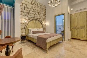 A bedroom with a stone wall, a bed with a wooden headboard, a chandelier, a wooden wardrobe, and a view through a door.