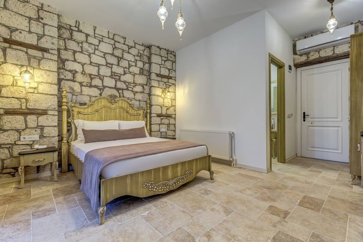 Un dormitorio con pared de piedra, una cama con cabecera de madera, una mesita de noche, un radiador y una puerta.