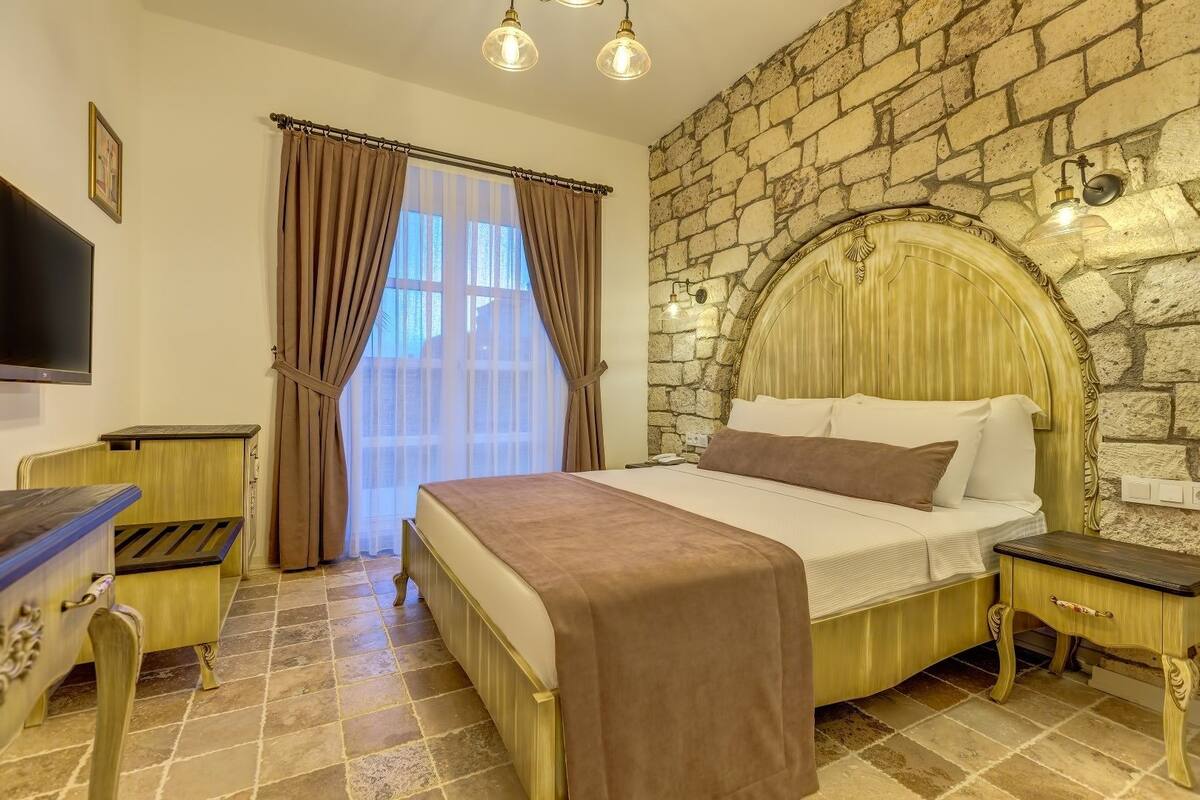 Un dormitorio con pared de piedra, una cama con cabecero, una mesita de noche, un televisor y cortinas.