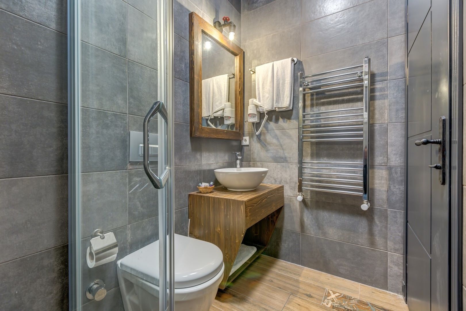 A modern bathroom with a glass shower enclosure, a wooden vanity with a sink, and a towel rack.