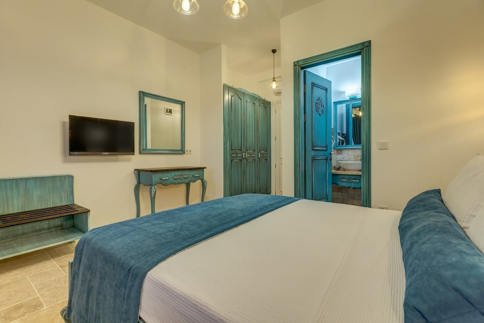 A bedroom with a bed, a TV, a dresser, and a door leading to a bathroom.