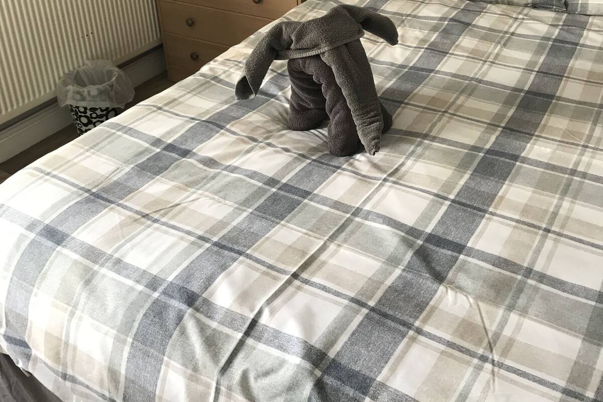 Quarto com colcha xadrez, cómoda de madeira com abajur e radiador.