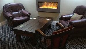 A cozy seating area with two leather armchairs, a wooden coffee table, and a built-in fireplace. - Black Bull Inn (Immingham)