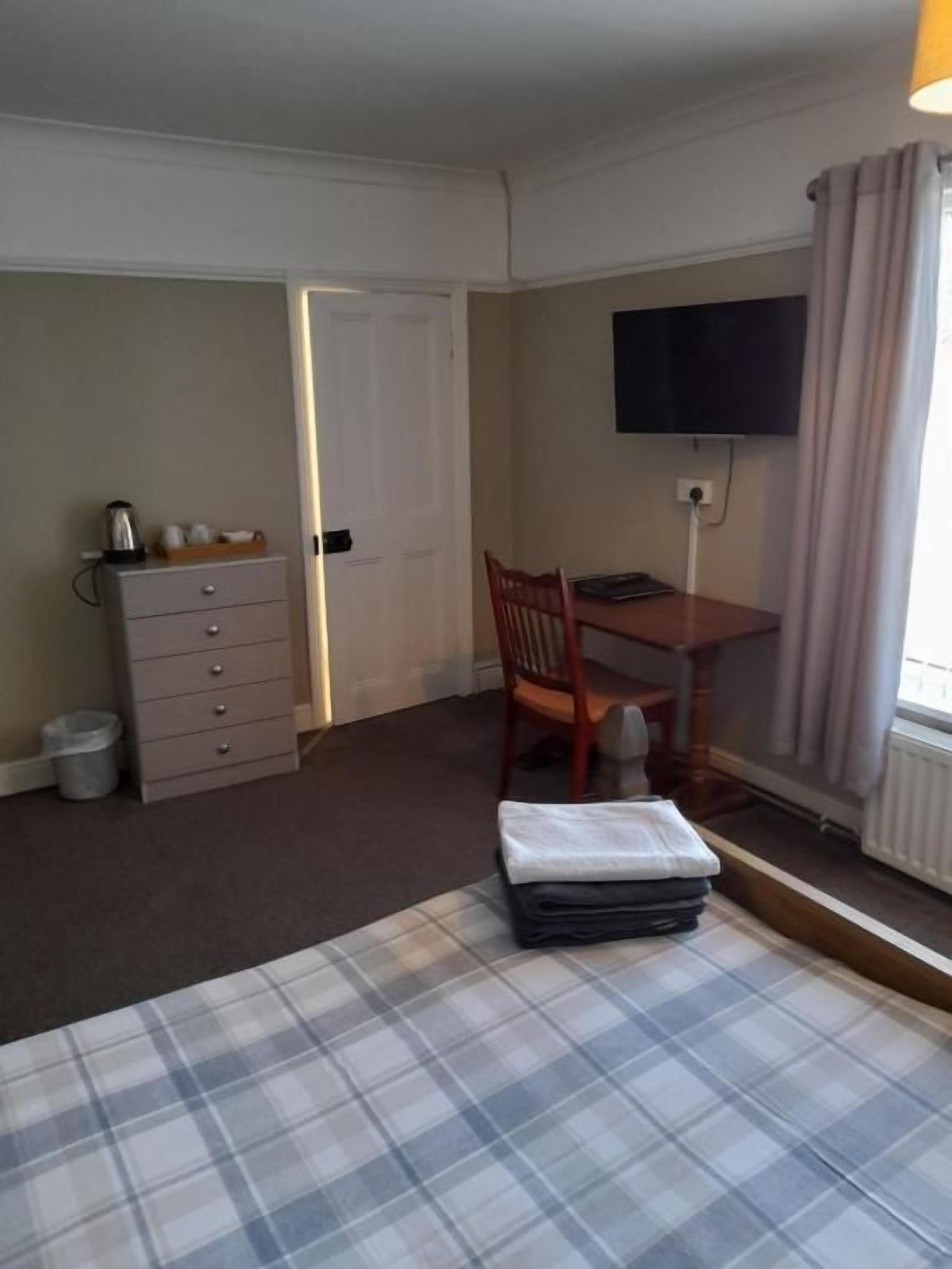 A hotel room with a bed, a desk, a chair, a television, and a dresser.