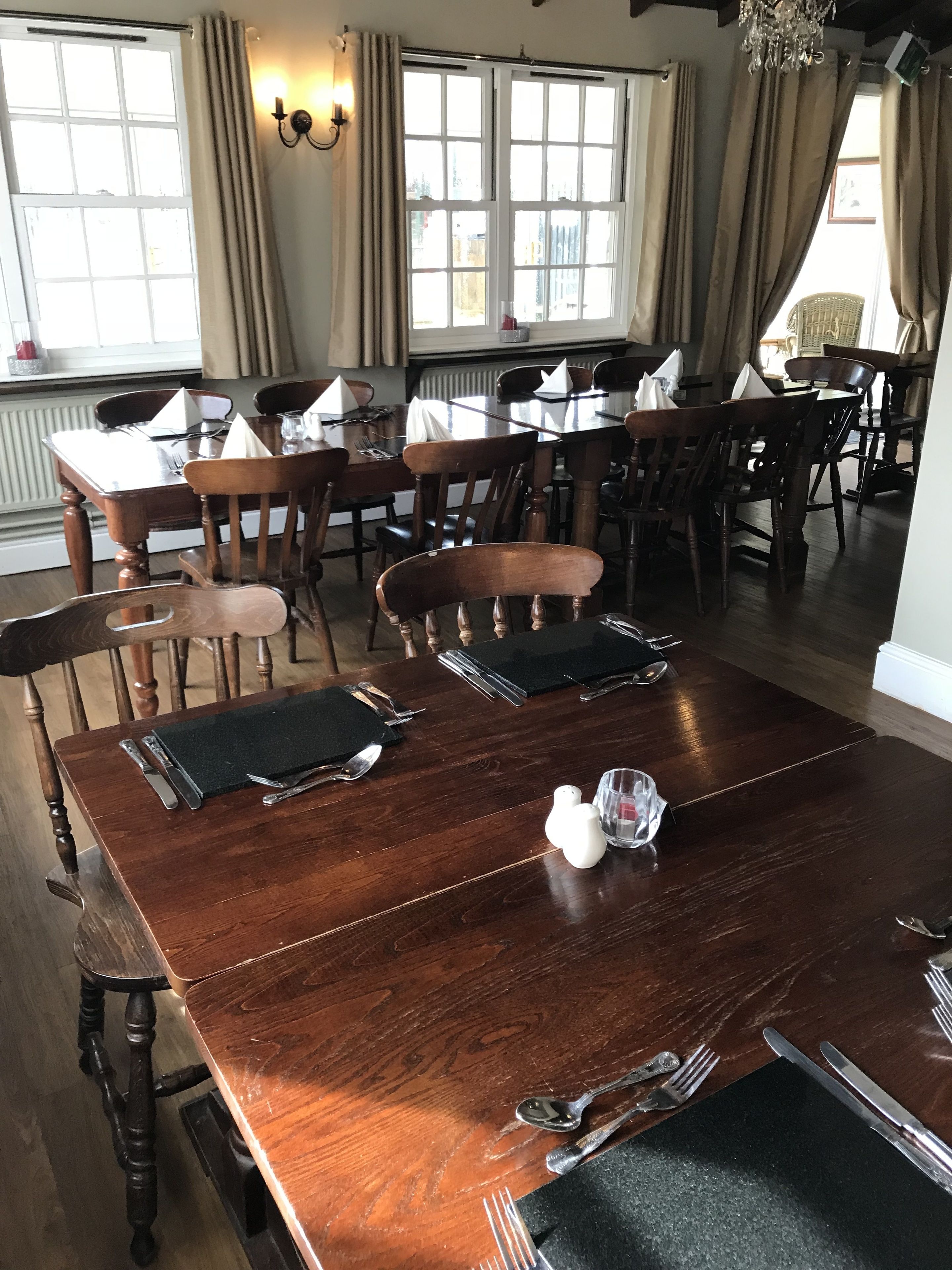 A dining area with wooden tables and chairs, set with cutlery and napkins.