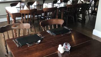 A dining area with wooden tables and chairs, set with cutlery and napkins.