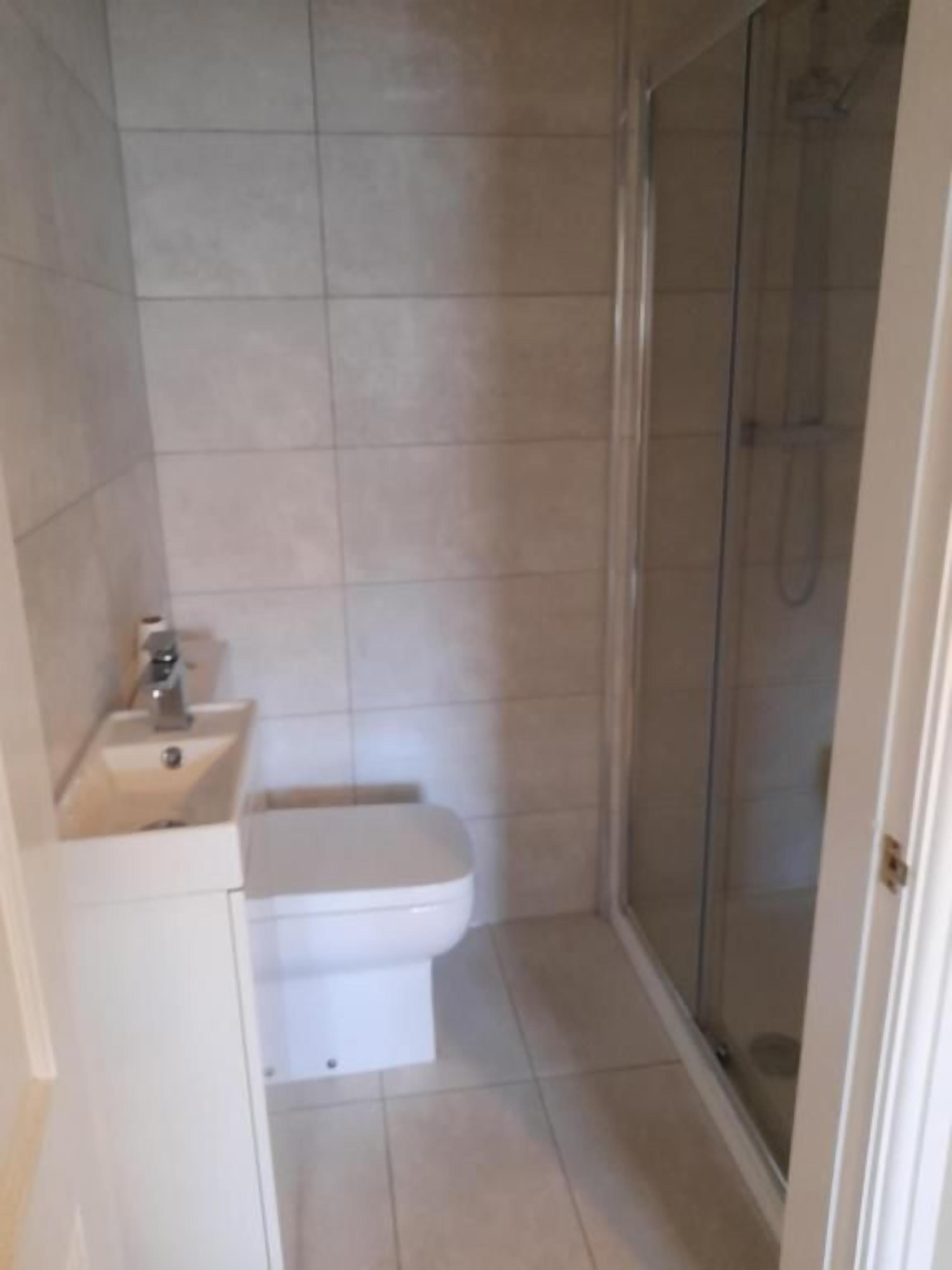 Baño pequeño con inodoro, lavamanos y cabina de ducha de vidrio.