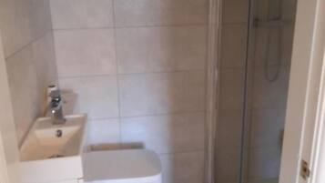 Baño pequeño con inodoro, lavamanos y cabina de ducha de vidrio.