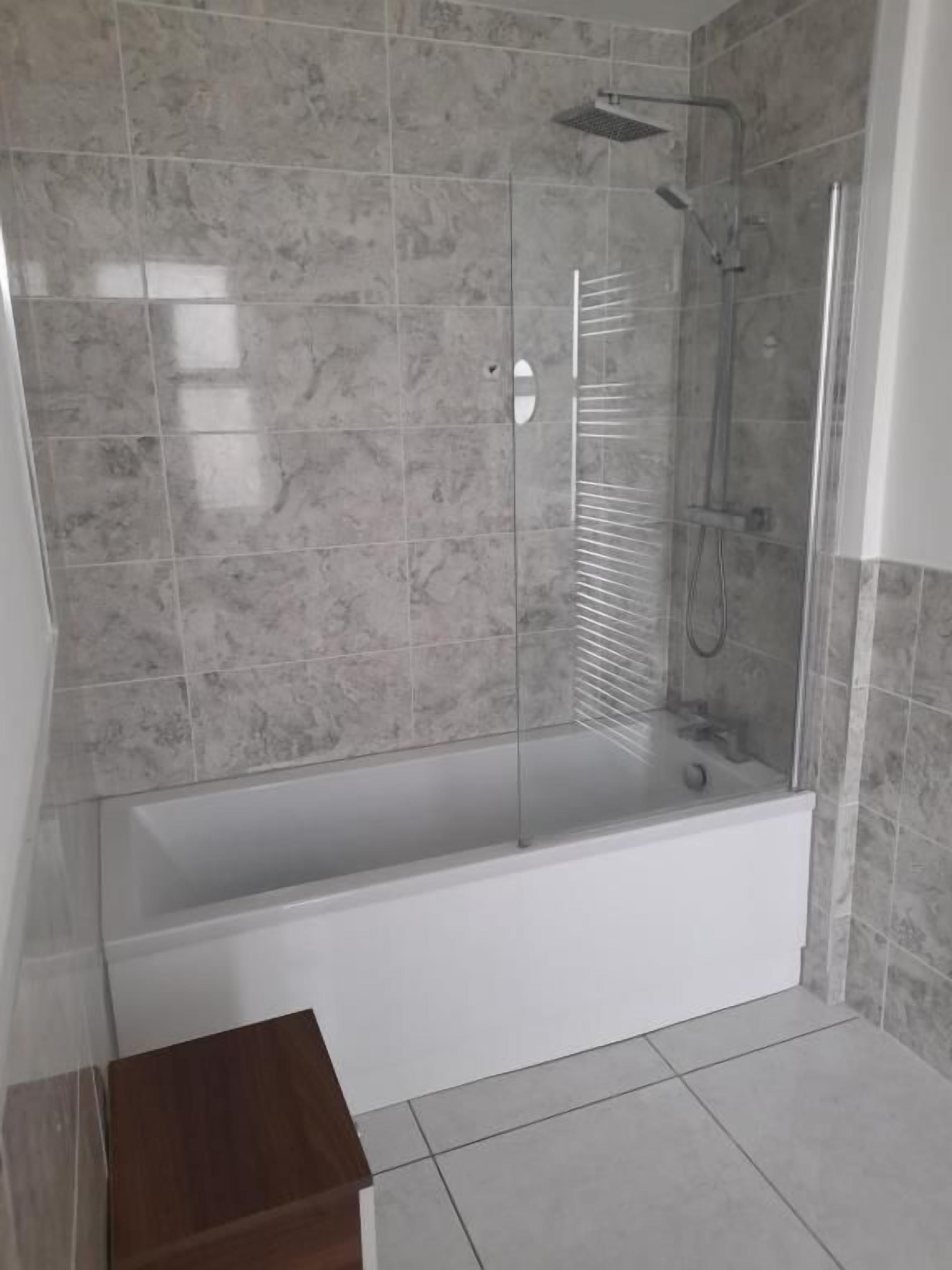 A bathroom with a glass-enclosed shower, a white bathtub, and a tiled floor.
