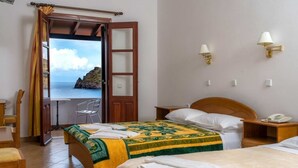 Ein Hotelzimmer mit einem Bett, einem Nachttisch mit Telefon, einem Stuhl und Meerblick durch eine geöffnete Tür.