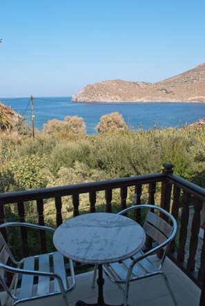 A balcony with a table and chairs overlooking a coastal landscape. - Asteri Hotel (Patmos)