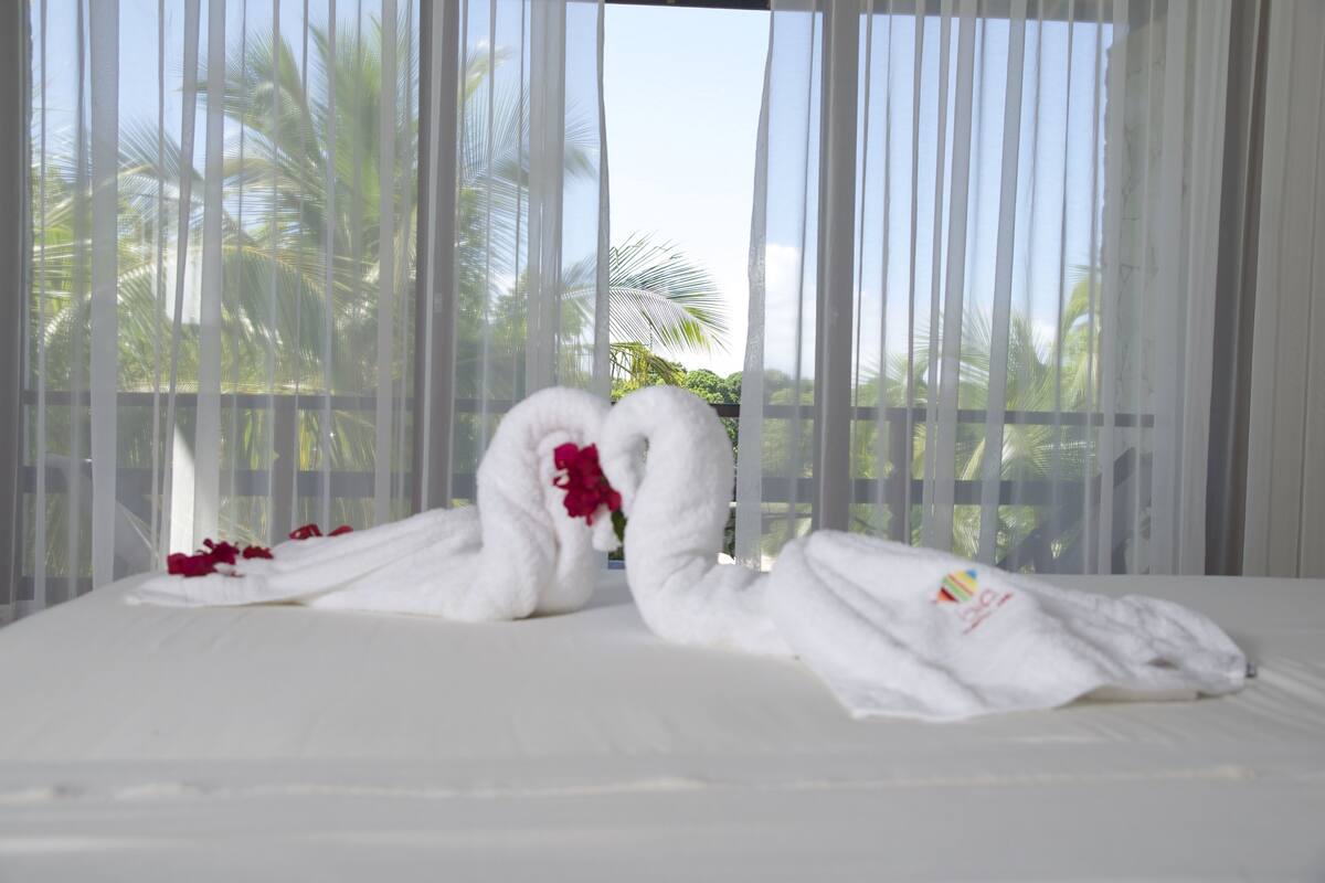 A bed with two white towels arranged in a heart shape, a red flower, and a logo on one towel.
