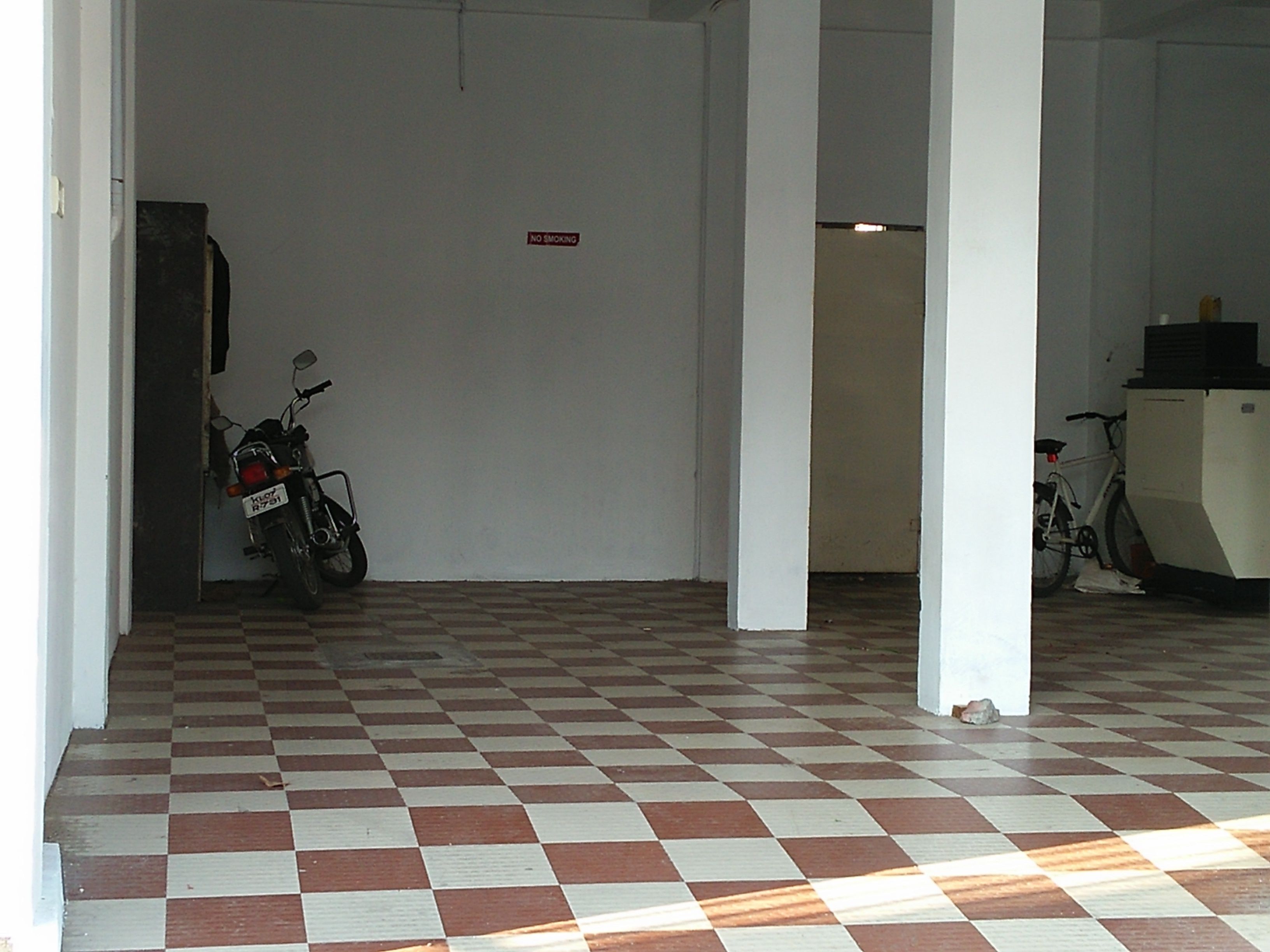 A checkered floor, a motorcycle, and a bicycle in a hallway with white walls and a 'No Smoking' sign.