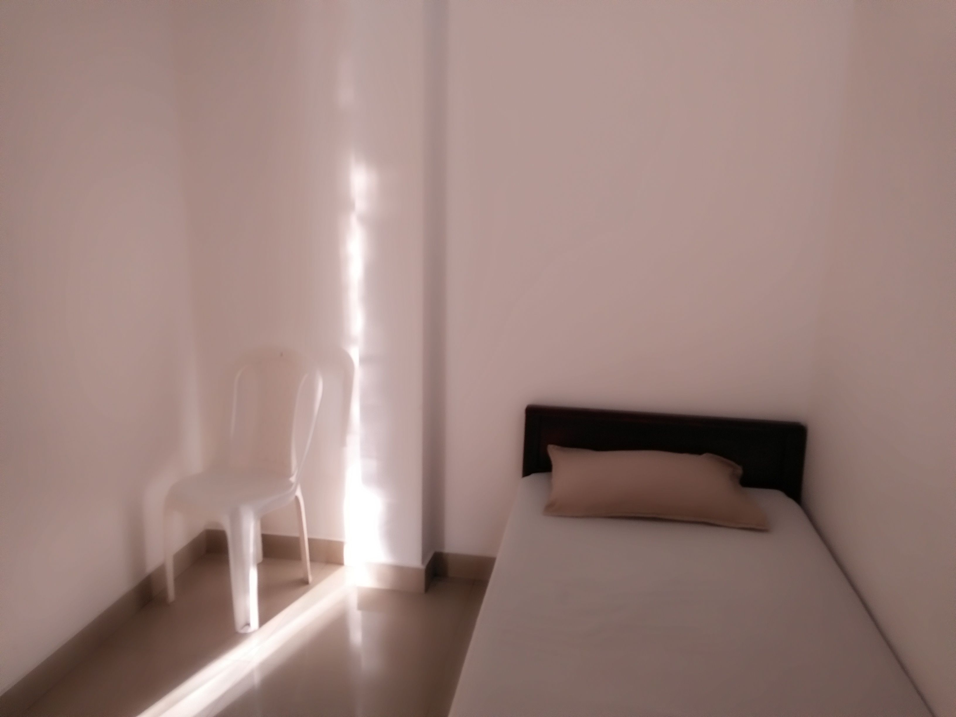 A room with a bed, a chair, and a window allowing natural light.