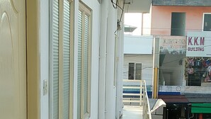 A corridor with a door on the left, a window with blinds, and a red basket on the floor.