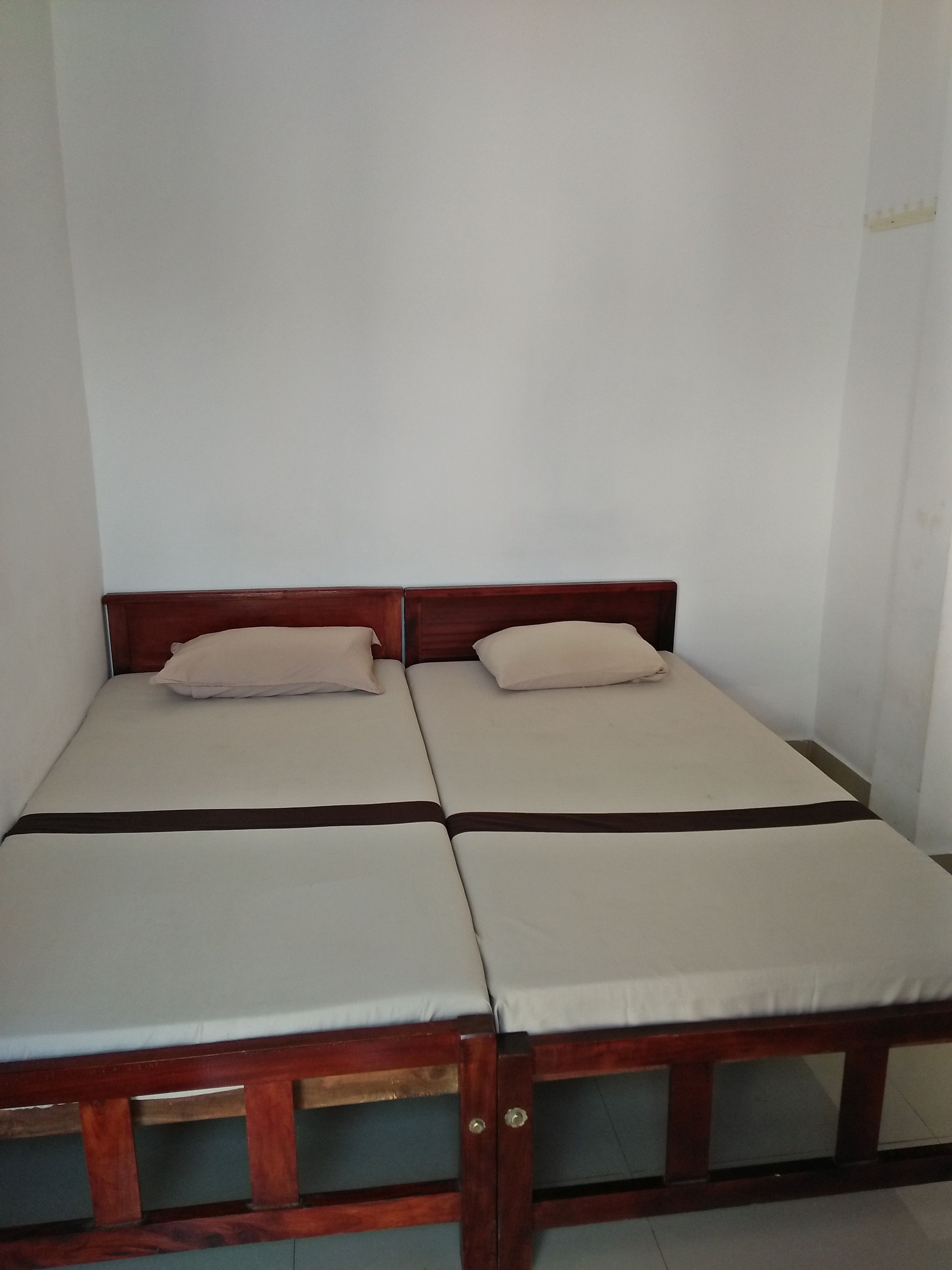 A room with two single beds, each with a wooden frame and white bedding.