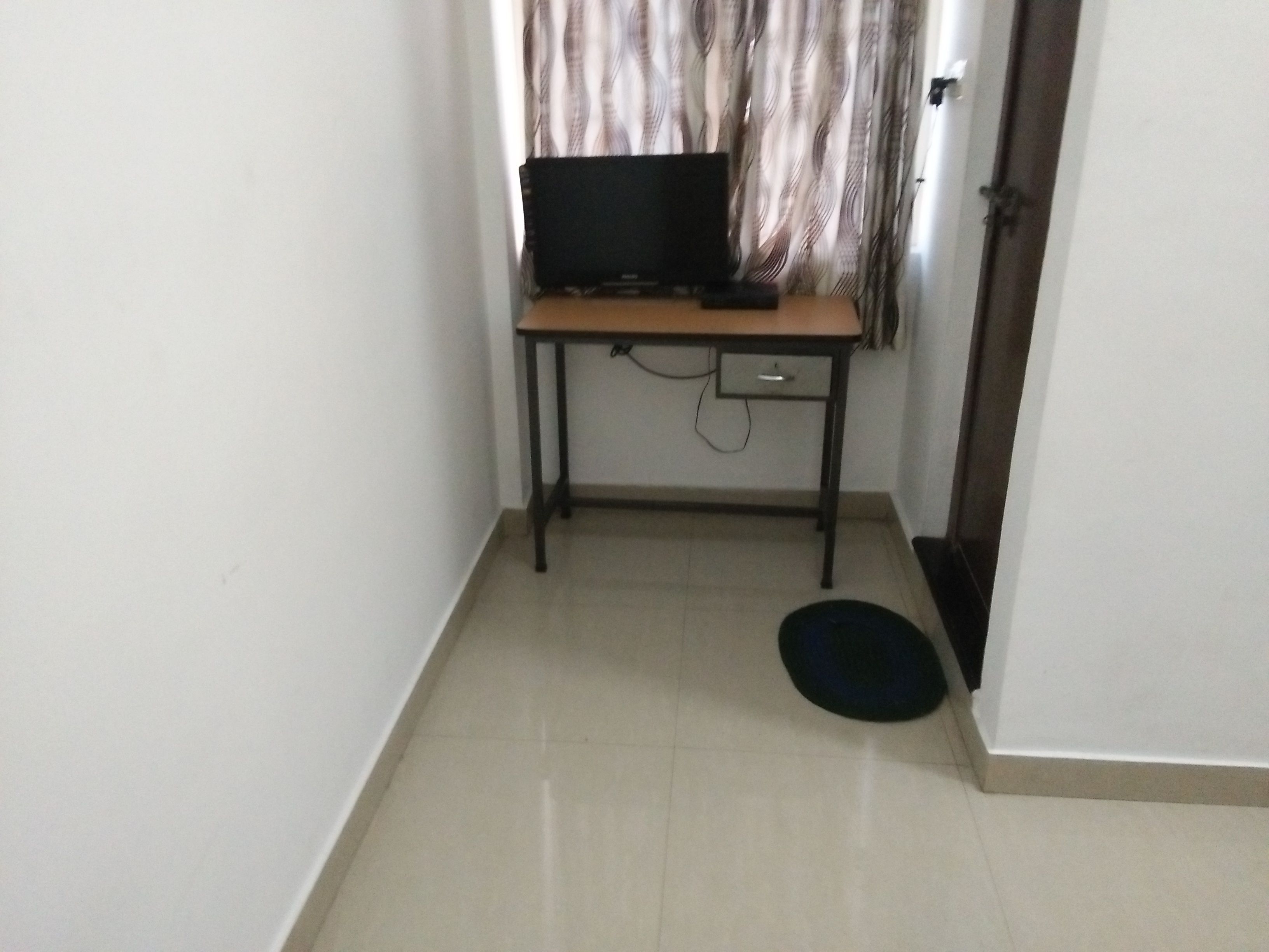 Une petite pièce comprenant un bureau, une chaise, un téléviseur et une porte.