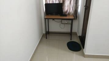 A small room with a desk, a chair, a television, and a door.