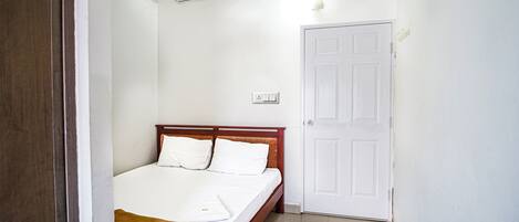 Ein Schlafzimmer mit einem hölzernen Bett, weißer Bettwäsche, einer weißen Tür und einer Klimaanlage an der Wand.