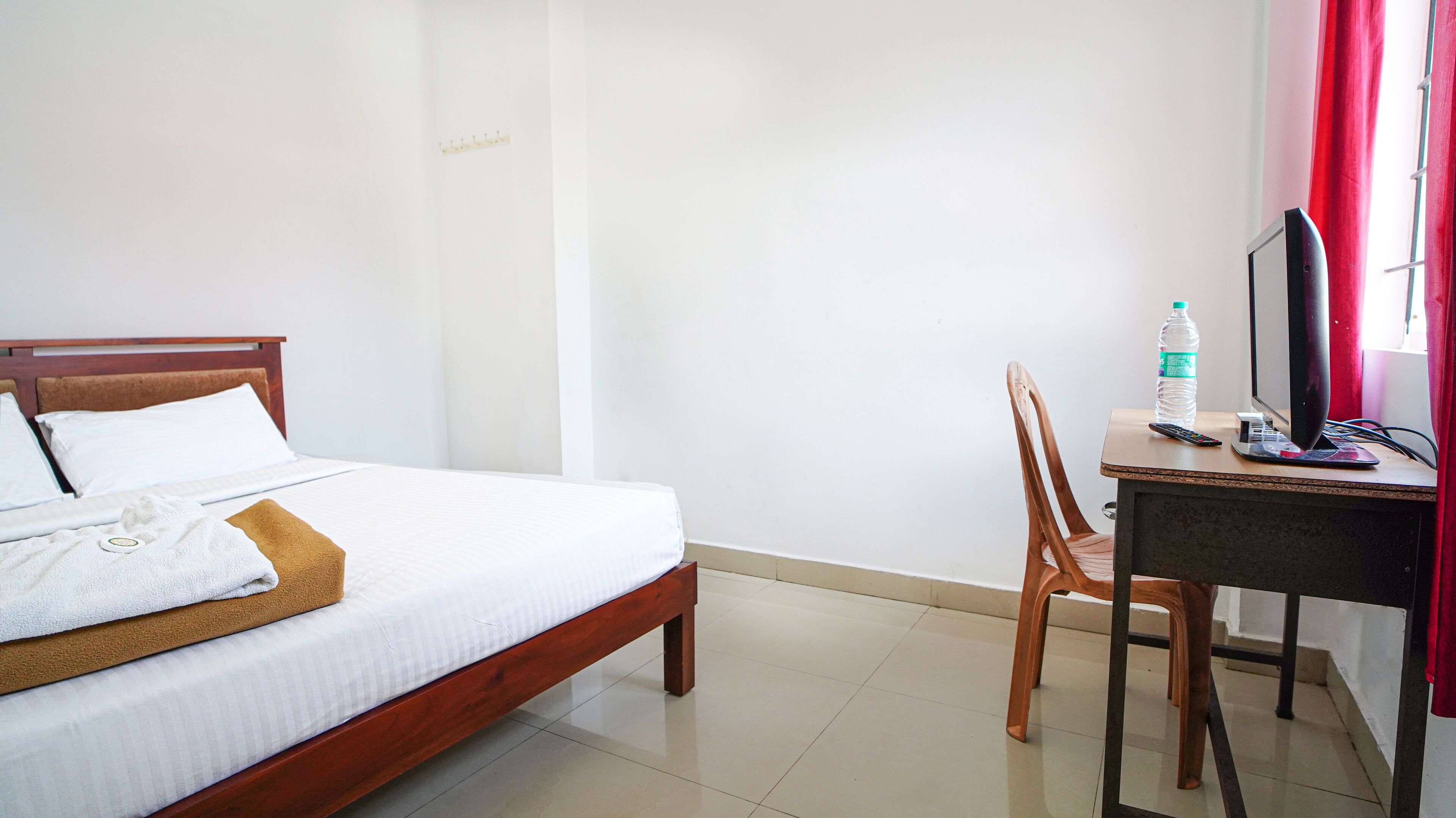 Habitación de hotel con cama, escritorio con computadora, una silla y ventana con cortinas rojas.