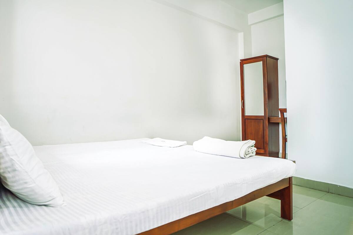 A single bed with white bedding, a wooden headboard, and a mirror on the wall.