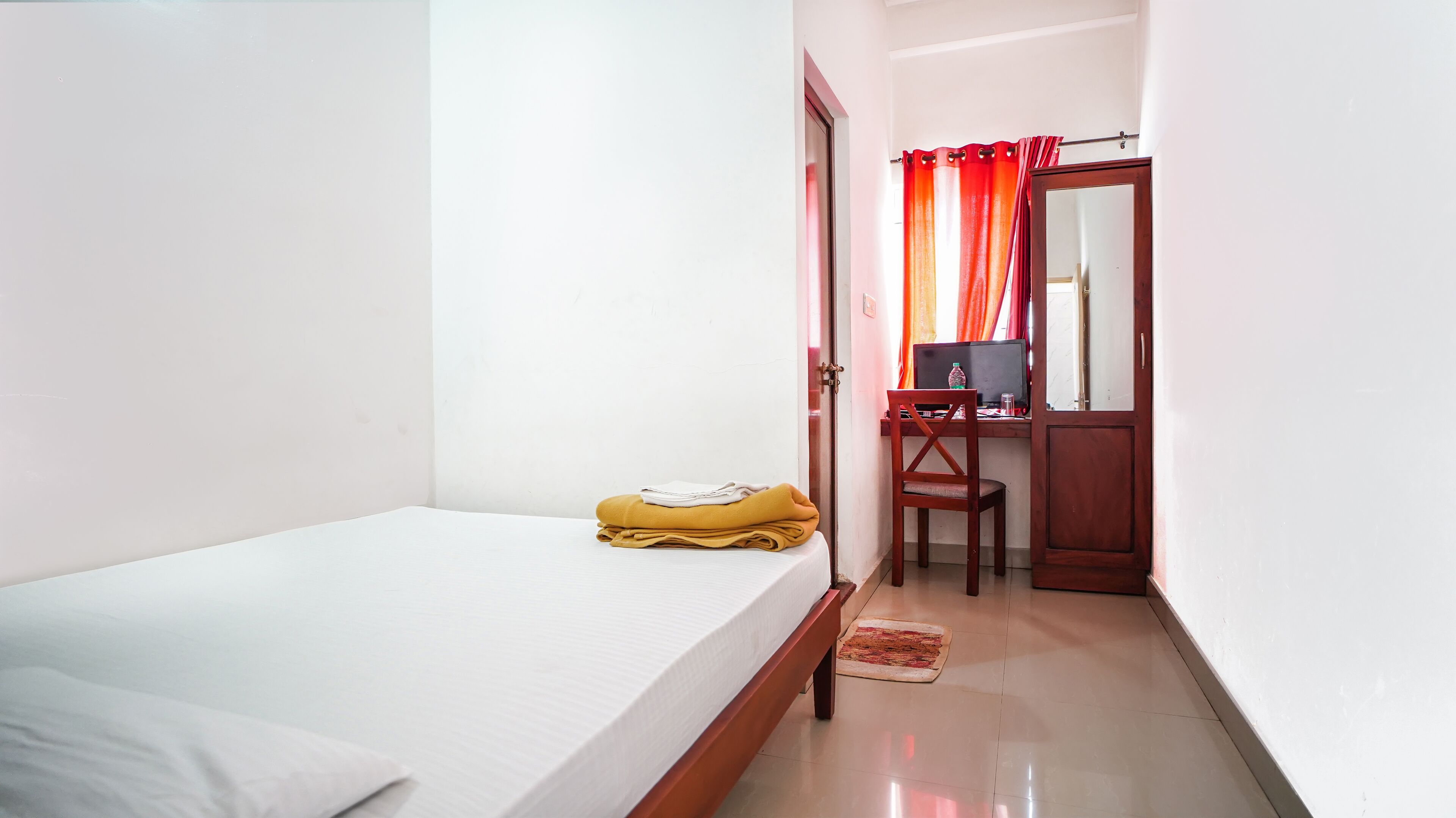 A small, clean room with a single bed, a desk with a computer, and a chair.