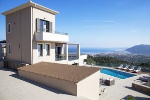 A modern two-story building with a rooftop pool, a balcony, and a view of a coastal city and mountains. - Alivia Lefkas (Lefkada)