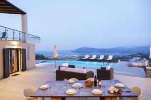 An outdoor dining area with a pool, lounge chairs, and a view of the city and mountains. - Alivia Lefkas (Lefkada)