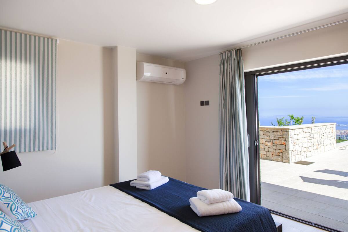 A hotel room with a bed, a view of the sea, and an air conditioning unit.