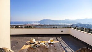 A terrace with a table set for breakfast, overlooking a scenic view of mountains and a city. - Alivia Lefkas (Lefkada)